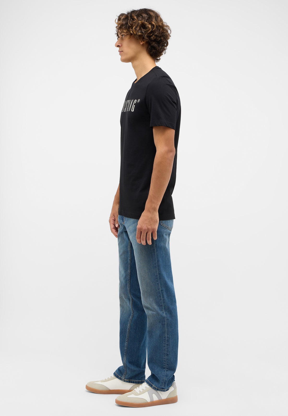 Tricou Austin negru, lateral, imprimeu alb-crem vizibil parțial, purtat cu blugi și pantofi sport